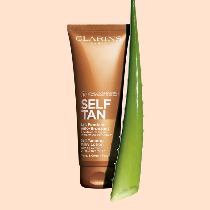 Pakkebilde av en tube med Clarins Self Tanning Milky Lotion i nærheten av en bit med aloe vera mot en lys oransje bakgrunn.