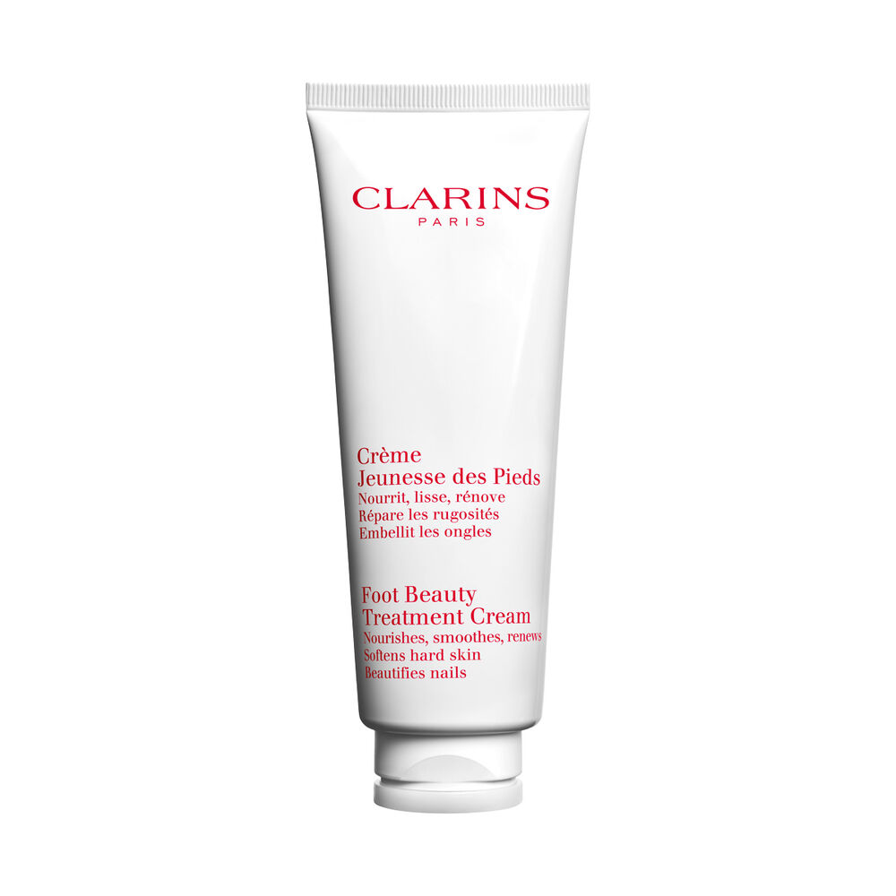 Pakkebilde av en flaske med Clarins Foot Beauty Treatment Cream i n&aelig;rheten av noen shean&oslash;tter mot en hvit bakgrunn.