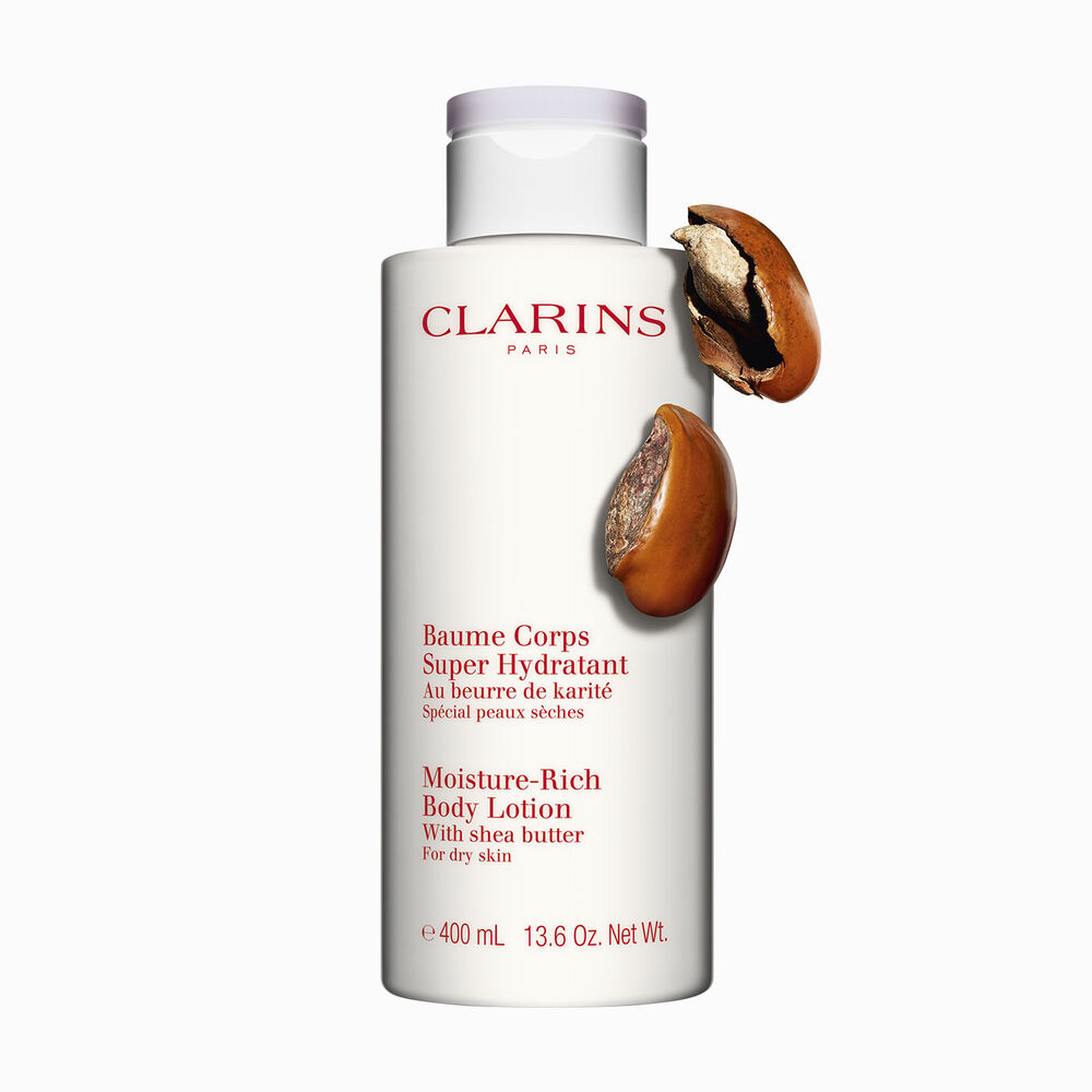 Pakkebilde av en flaske med Clarins Moisture-Rich Body Lotion i nærheten av noen sheanøtter mot en hvit bakgrunn.