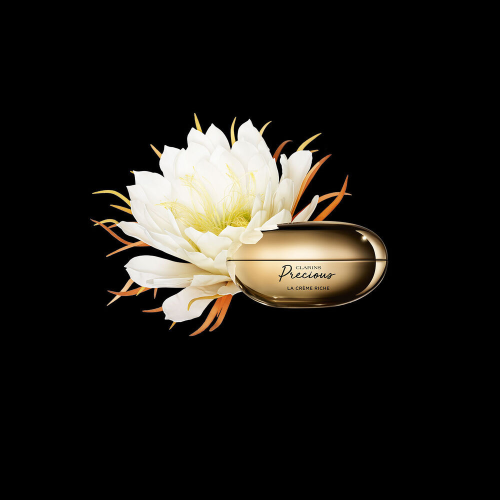 Pakkebilde av Clarins Precious Rich Cream i nærheten av blomsten nattens dronning mot en mørk bakgrunn.