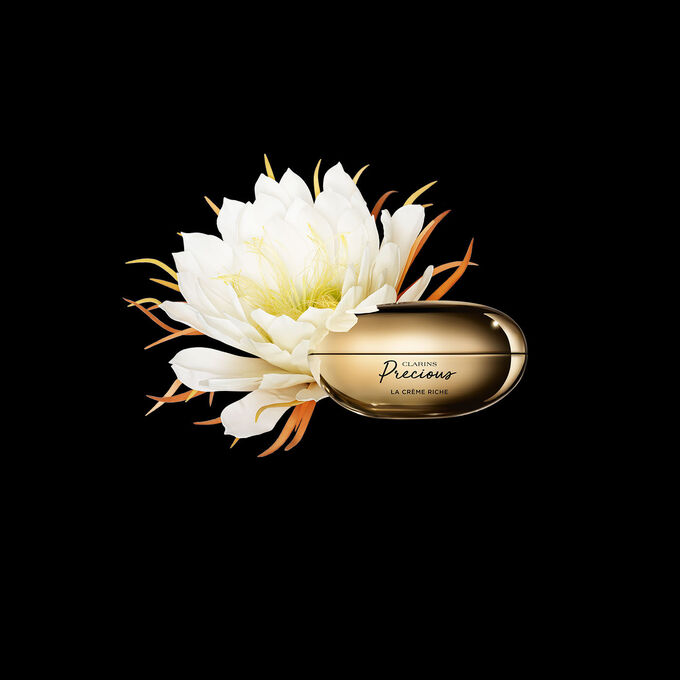 Pakkebilde av Clarins Precious Rich Cream i nærheten av blomsten nattens dronning mot en mørk bakgrunn.