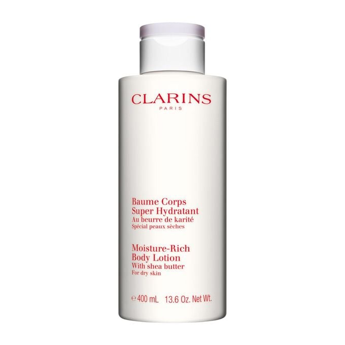 Pakkebilde av en flaske med Clarins Moisture-Rich Body Lotion i n&aelig;rheten av noen shean&oslash;tter mot en hvit bakgrunn.