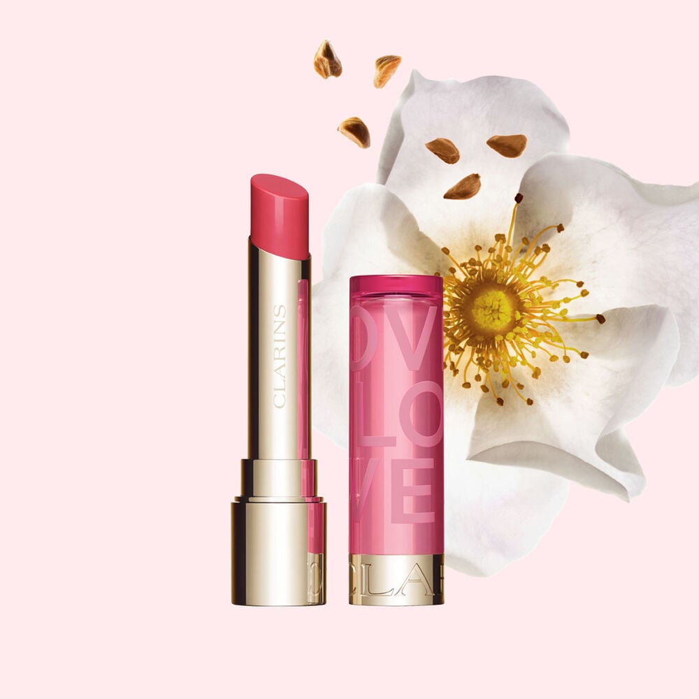 Packshot av Lip Balm Limited Edition Love Collection foran en rose p&aring; en lys rosa bakgrunn som fremhever den livfulle fargen.