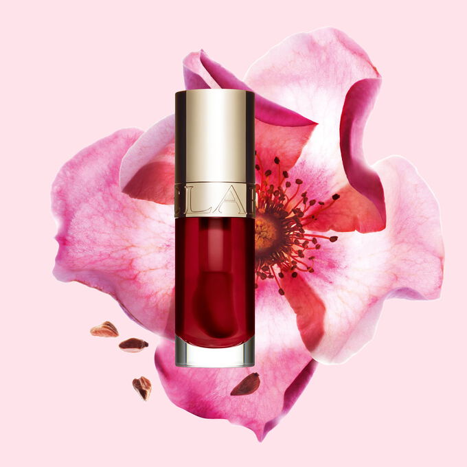 Packshot av Clarins Lip Comfort Oil i Cherry, plassert ved siden av en nyperose p&aring; en lys rosa bakgrunn.