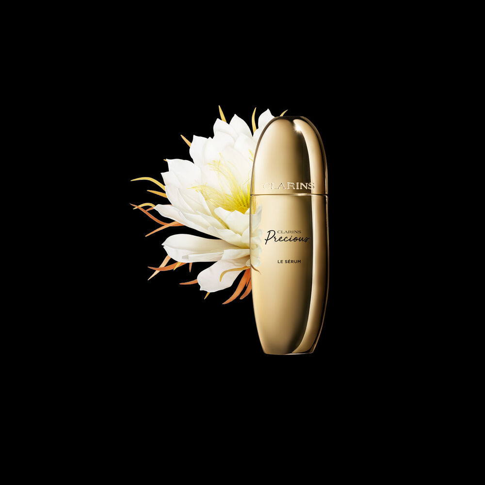 Pakkebilde av Clarins Precious Serum i nærheten av blomsten nattens dronning mot en mørk bakgrunn.