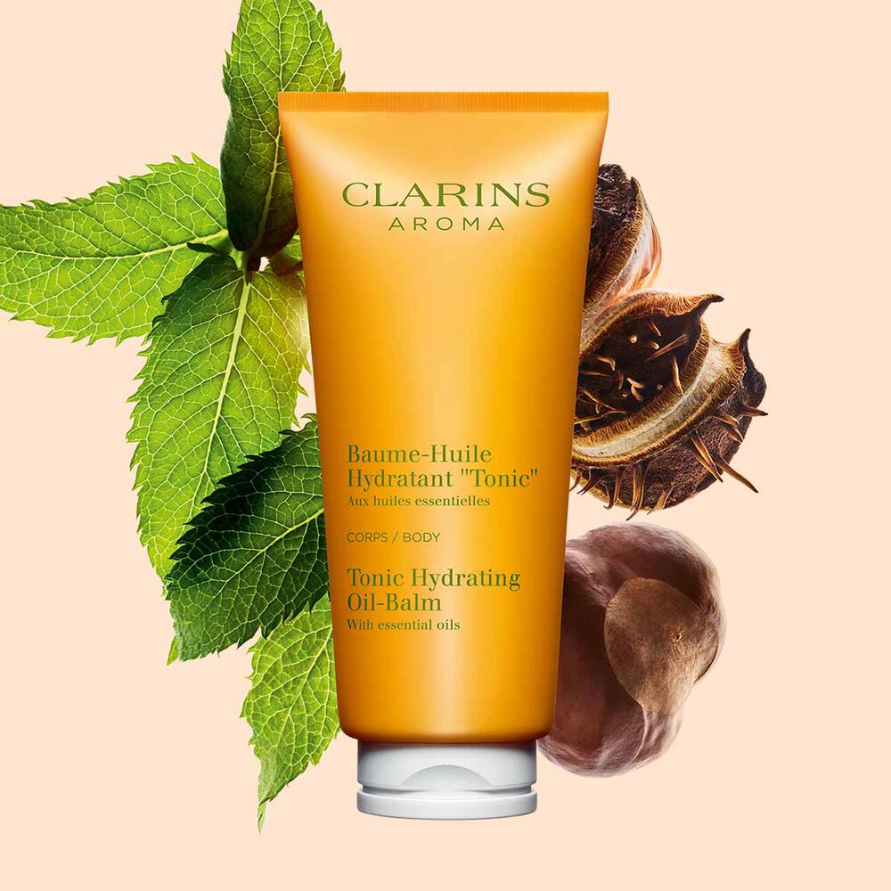 Pakkebilde av en tube med Clarins Tonic Hydrating Oil-Balm, i nærheten av mynteblader og sheafrø mot en ferskenfarget bakgrunn.