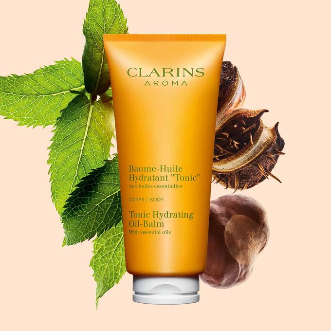 Pakkebilde av en tube med Clarins Tonic Hydrating Oil-Balm, i nærheten av mynteblader og sheafrø mot en ferskenfarget bakgrunn.