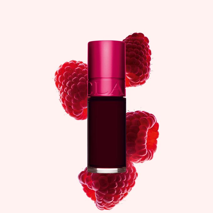 Packshot av Clarins Pink Water Lip Stain i nyanse 04, plassert ved siden av bringebær på en lys rosa bakgrunn.