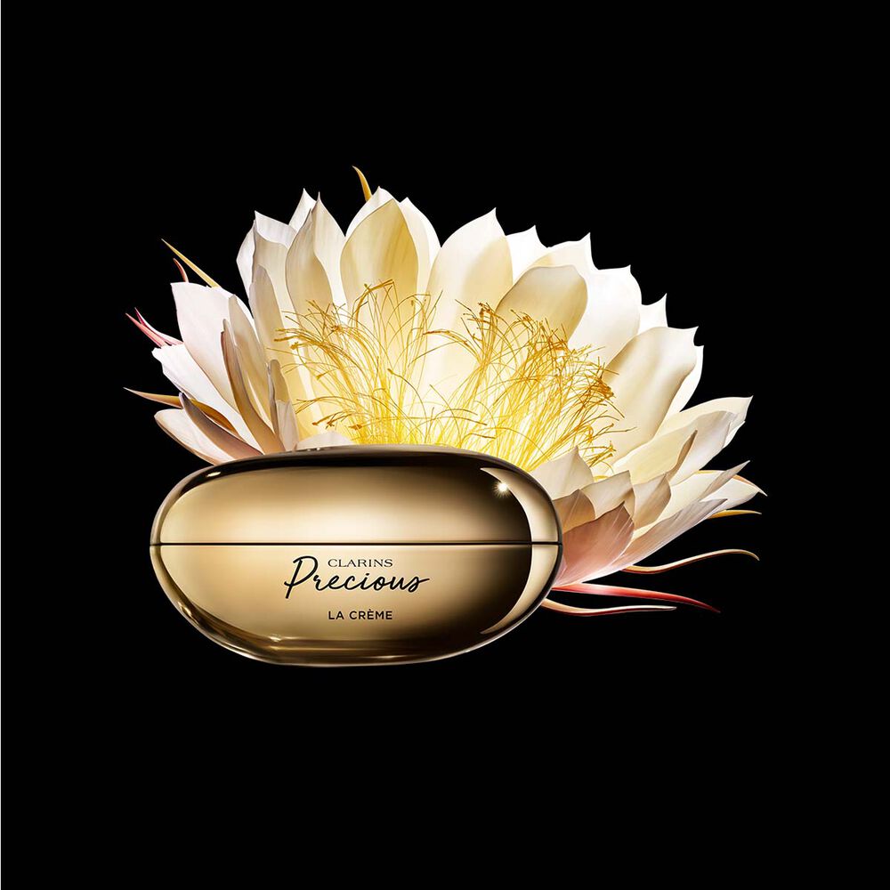 Pakkebilde av Clarins Precious Soft Cream i nærheten av blomsten nattens dronning mot en mørk bakgrunn.