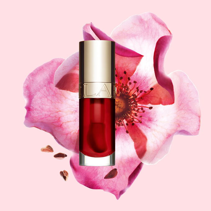 Packshot av Clarins Lip Comfort Oil Strawberry, plassert ved siden av en nyperose p&aring; en lys rosa bakgrunn.