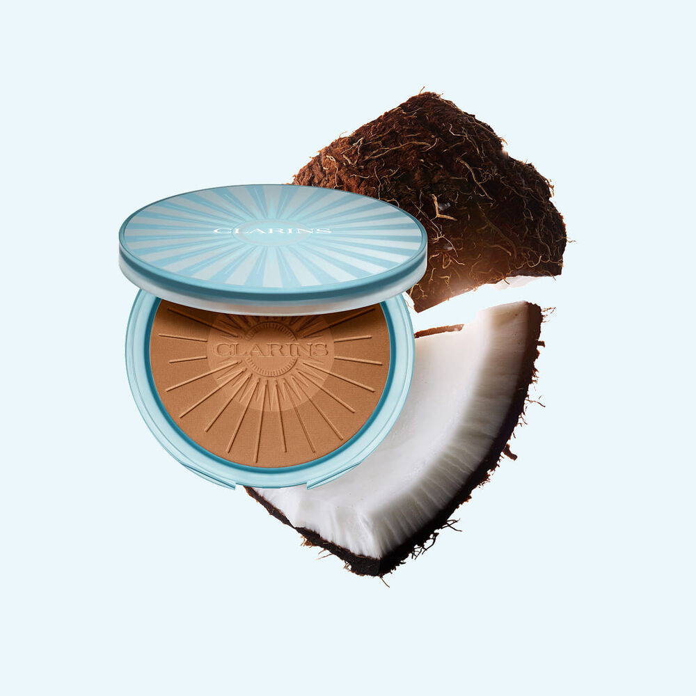 Packshot av Summer Bronzing Powder omgitt av kokos som illustrerer n&oslash;kkelingrediensen for en naturlig, solkysset gl&oslash;d