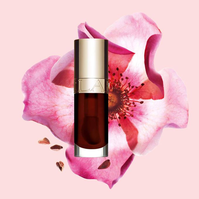 Packshot av Clarins Lip Comfort Oil Chocolate, plassert ved siden av en nyperose p&aring; en lys rosa bakgrunn.