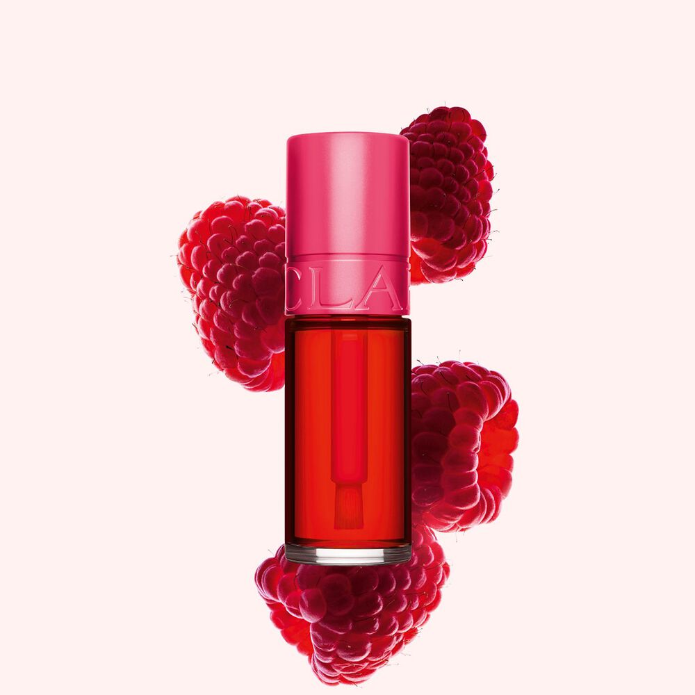 Packshot av Clarins Fushia Water Lip Stain i nyanse 01, plassert ved siden av bringebær på en lys rosa bakgrunn.