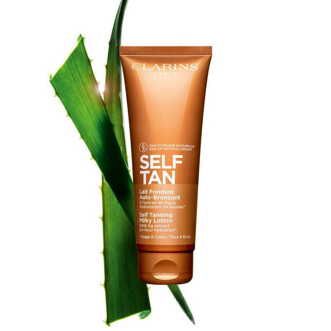 Pakkebilde av en tube med Clarins Self Tanning Milky Lotion i n&aelig;rheten av en bit med aloe vera mot en lys oransje bakgrunn.