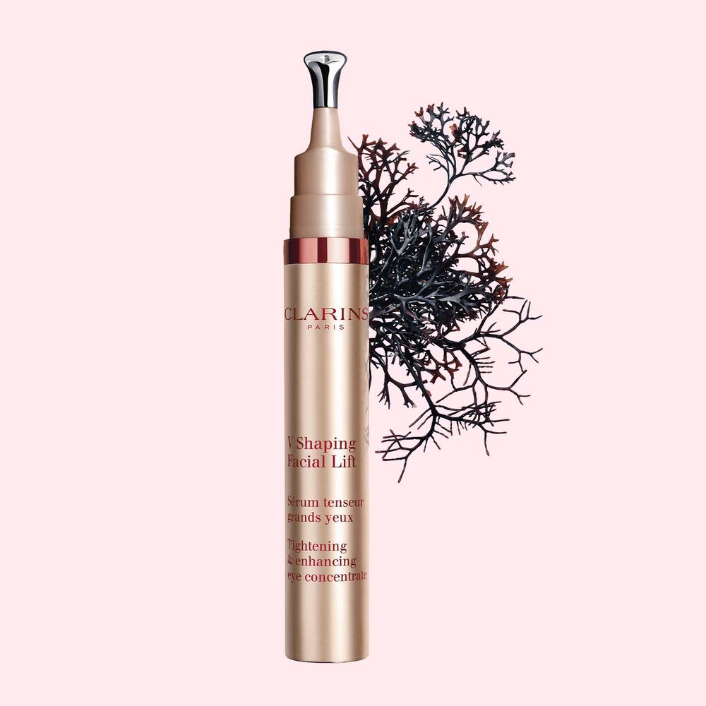 Pakkebilde av en tube med V Shaping Facial Lift Eye fra Clarins i nærheten av krusflik mot en lys rosa bakgrunn.