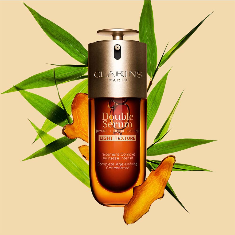 En 50 ml flaske med Clarins Double Serum Light Texture blant gurkemeie og blader fra kjemperør fra Provence mot en oransje bakgrunn.