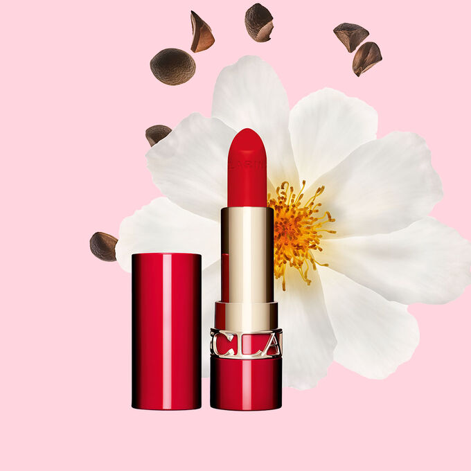 Packshot av Clarins matt leppestift Joli Rouge 792 V, ved siden av kamelia-blomst og sheafr&oslash; p&aring; rosa bakgrunn.