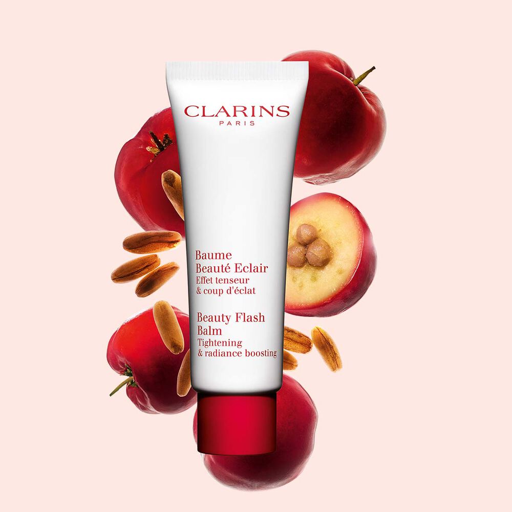 Pakkebilde av en tube med Clarins Beauty Flash Balm i nærheten av acerolafrø mot en ferskenfarget bakgrunn.