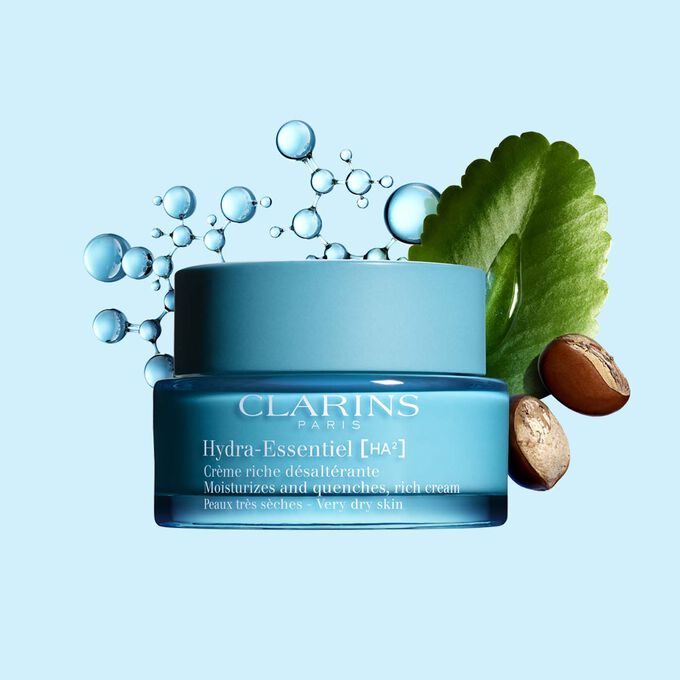 Pakkebilde av Clarins Hydra-Essentiel Rich Cream i nærheten av noen sheanøtter og kalanchoeblad mot en blå bakgrunn.
