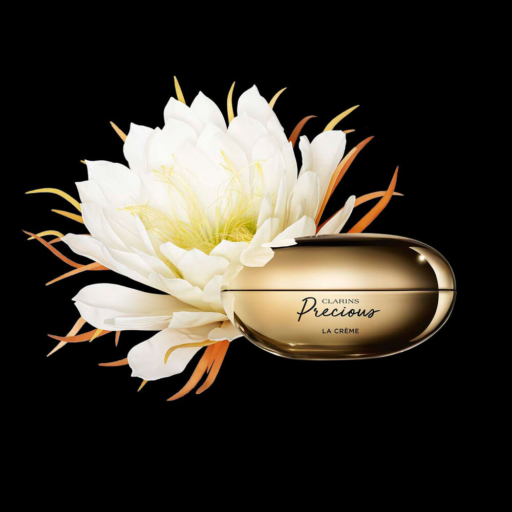 Pakkebilde av Clarins Precious Soft Cream i nærheten av blomsten nattens dronning mot en mørk bakgrunn.