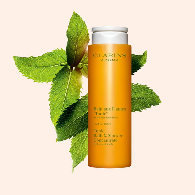 Pakkebilde av Clarins Tonic Bath and Shower Concentrate gel, i n&aelig;rheten av mynte- og rosmarinblader mot en oransje bakgrunn.