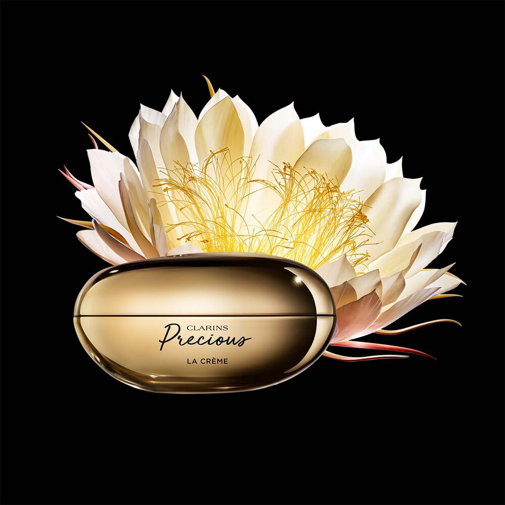 Pakkebilde av Clarins Precious Soft Cream i nærheten av blomsten nattens dronning mot en mørk bakgrunn.