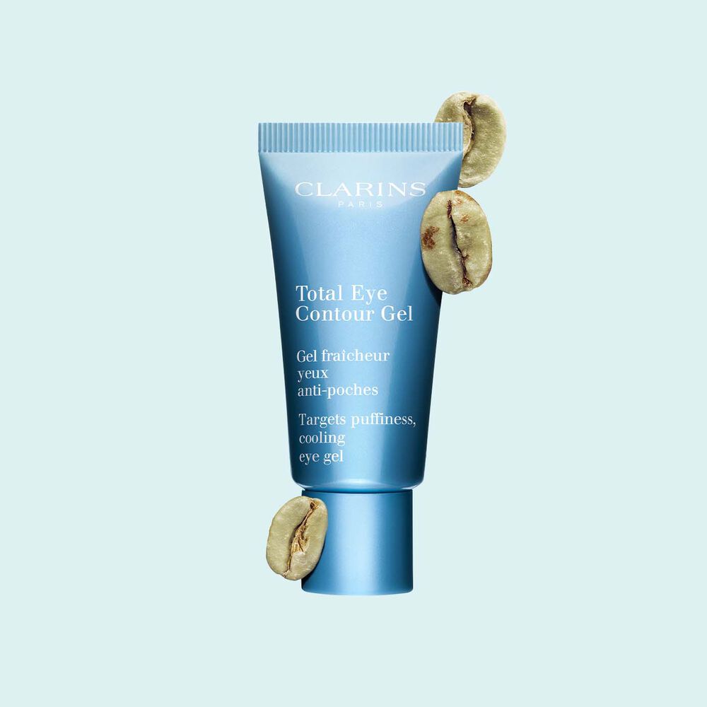 Pakkebilde av en tube med Total Eye Contour Gel fra Clarins i nærheten av kaffebønner mot en blå bakgrunn.