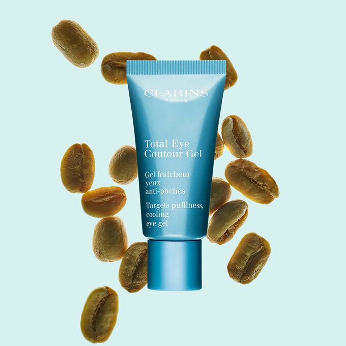 Pakkebilde av en tube med Total Eye Contour Gel fra Clarins i nærheten av kaffebønner mot en blå bakgrunn.