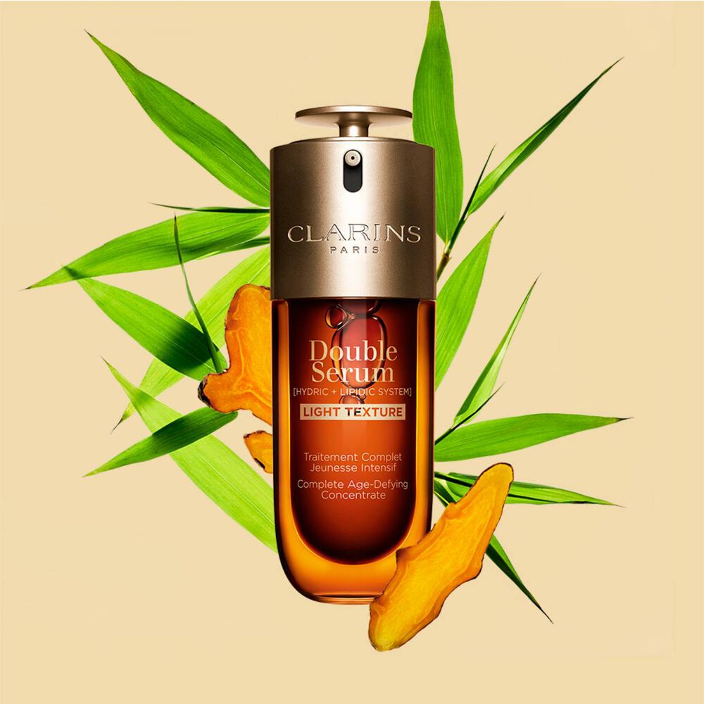 En 50 ml flaske med Clarins Double Serum Light Texture blant gurkemeie og blader fra kjemperør fra Provence mot en oransje bakgrunn.