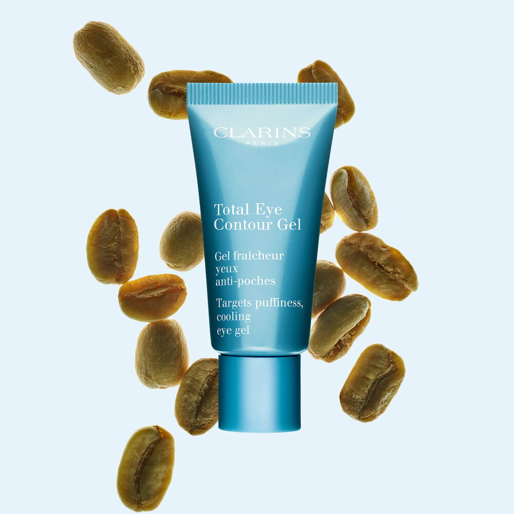 Pakkebilde av en tube med Total Eye Contour Gel fra Clarins i n&aelig;rheten av kaffeb&oslash;nner mot en bl&aring; bakgrunn.