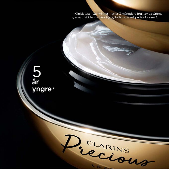 Pakkebilde av Clarins Precious Soft Cream mot en mørk bakgrunn med tekst som fremhever kraften til å få huden til å se fem år yngre ut