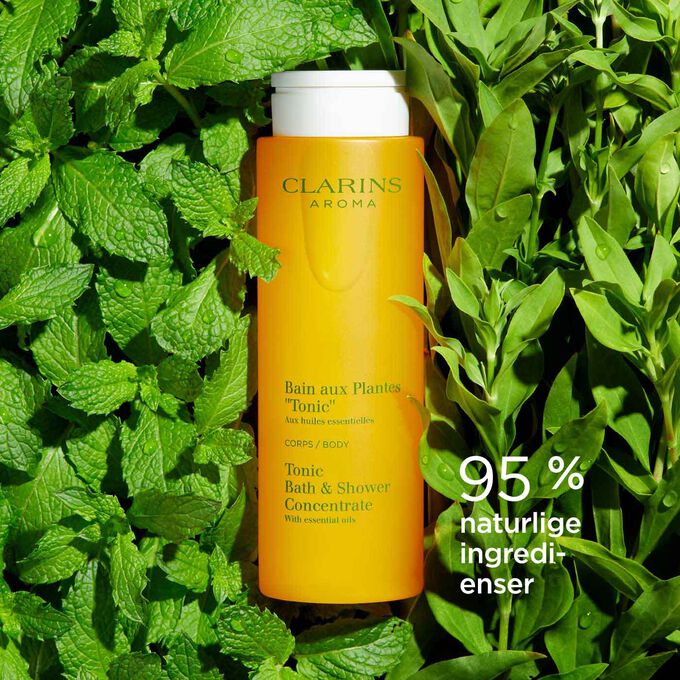 Flaske med Clarins Tonic Bath and Shower Concentrate blant mynte- og rosmarinblader for å illustrere de naturlige ingrediensene.