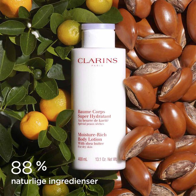 Flaske med Moisture-Rich Body Lotion omringet av sheanøtter og appelsiner, for å illustrere de naturlige ingrediensene.