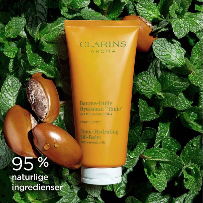 Tube med Clarins Tonic Hydrating Oil-Balm blant mynteblader og sheafrø for å illustrere de naturlige ingrediensene
